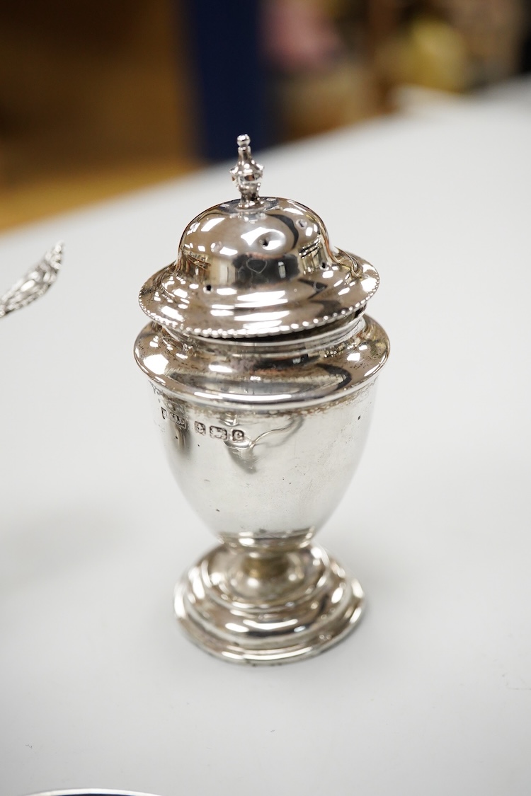 An ornate Edwardian silver oval mustard pot and matching spoon by Barker Brothers, Birmingham, 1902, length, 95mm, together with five other assorted silver condiments including a pair of pierced oval salts with blue glas